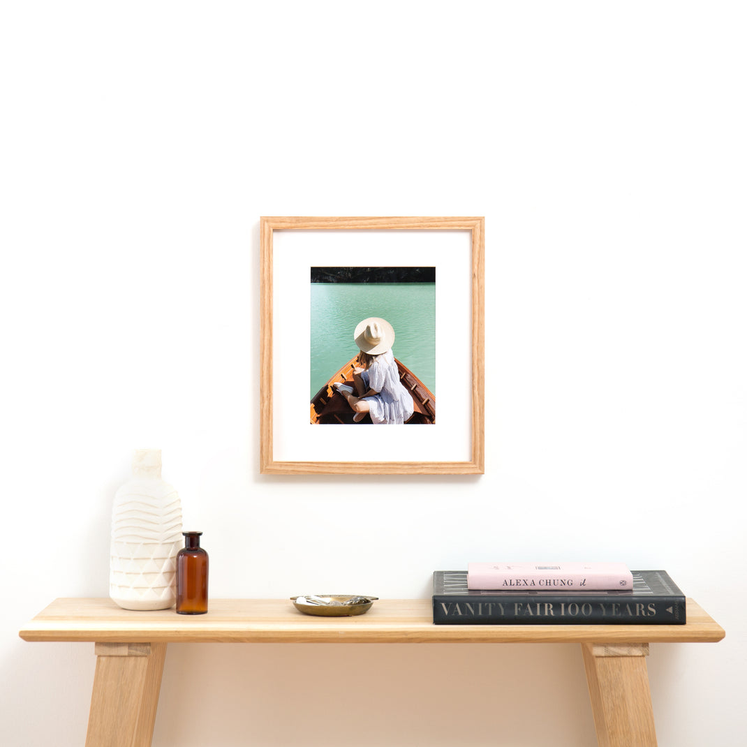 Photo of a woman wearing a hat in a boat on a lake framed in Ash Gallery with a white mat hanging on a white wall above an entry table