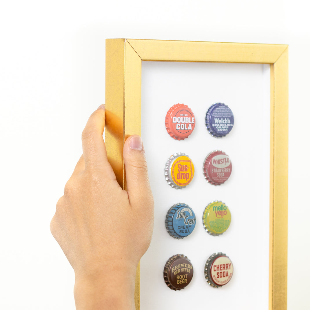top left corner of eight bottle caps framed in modern gold Dolly frame