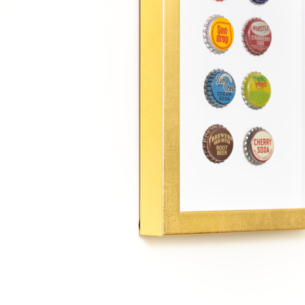 bottom left corner of eight bottle caps framed in modern gold Dolly frame