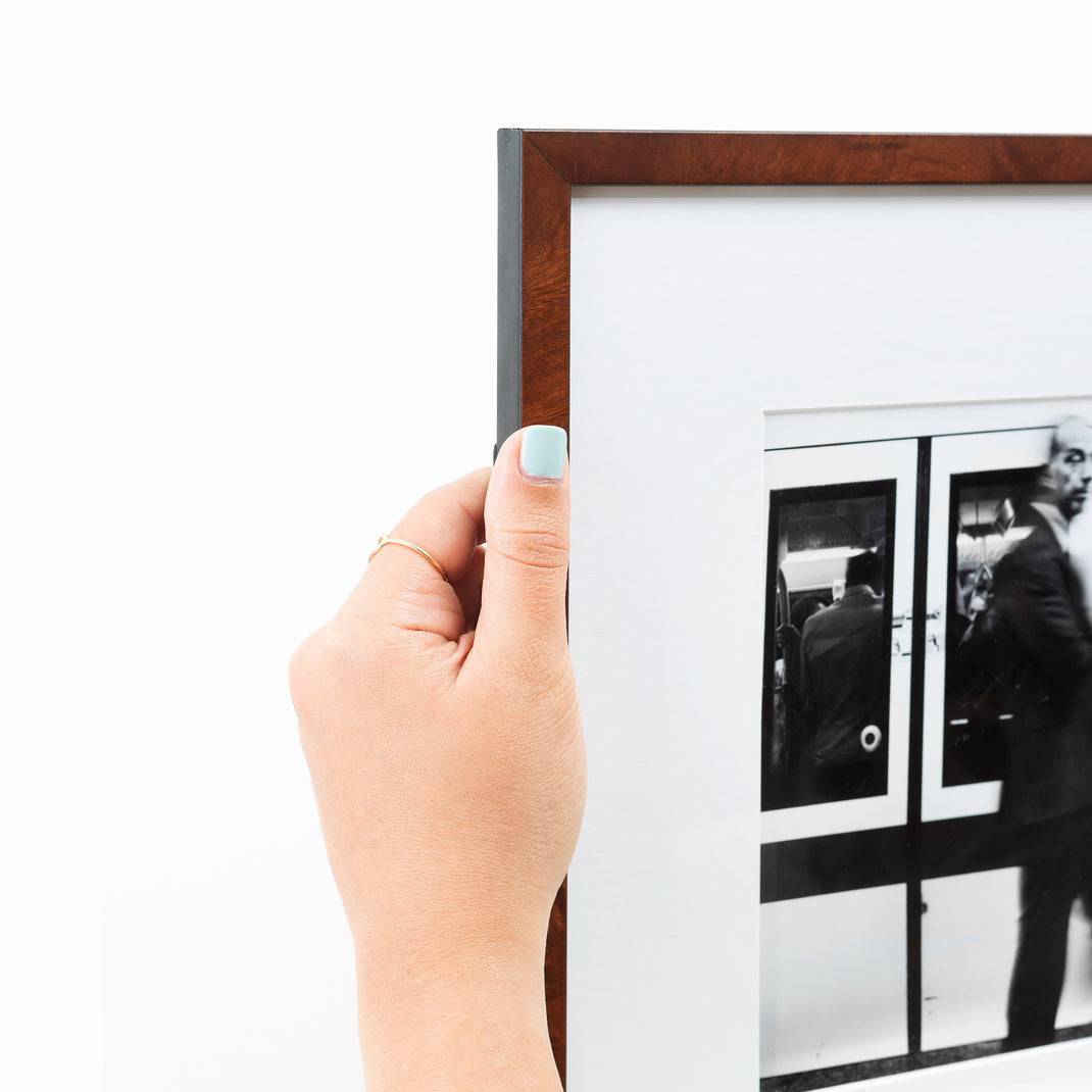 top left corner of blurry black and white photo of a man in front of a subway train framed in dark skinny burl wood Frederick frame with a white mat