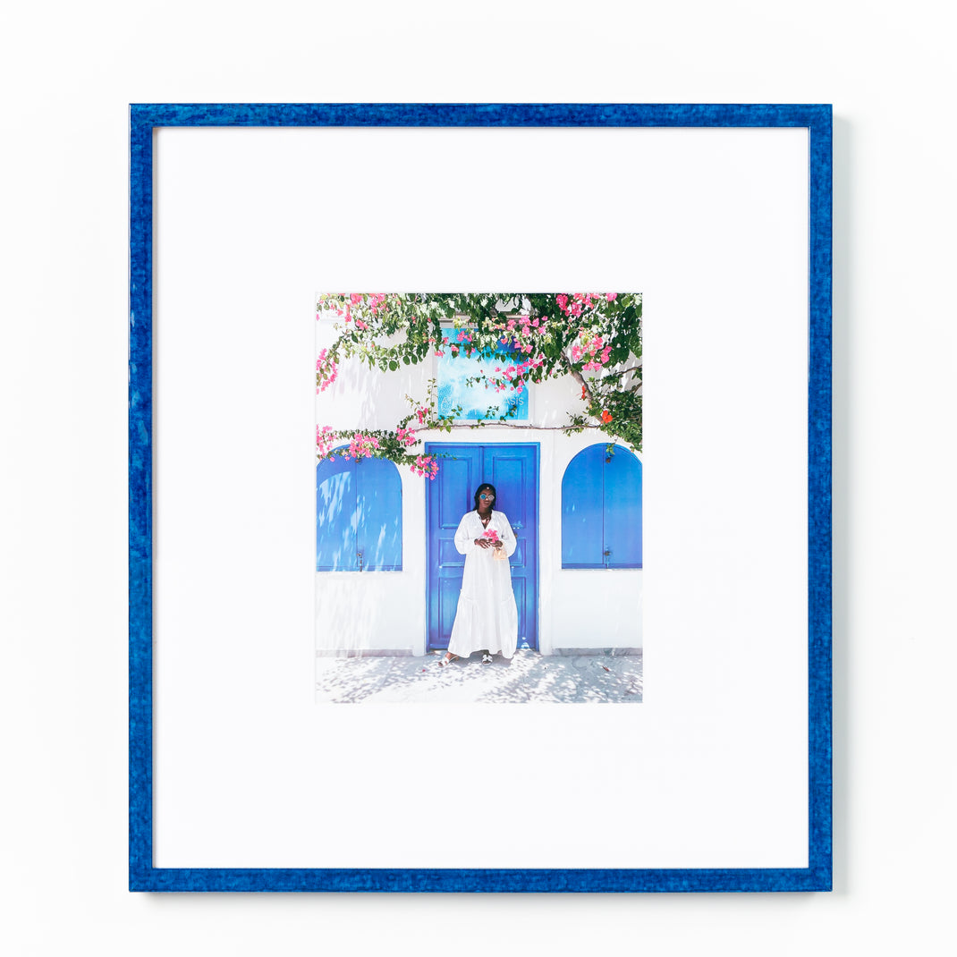 photo of a woman in front of a blue door framed in royal blue glazed Santorini frame with a white mat