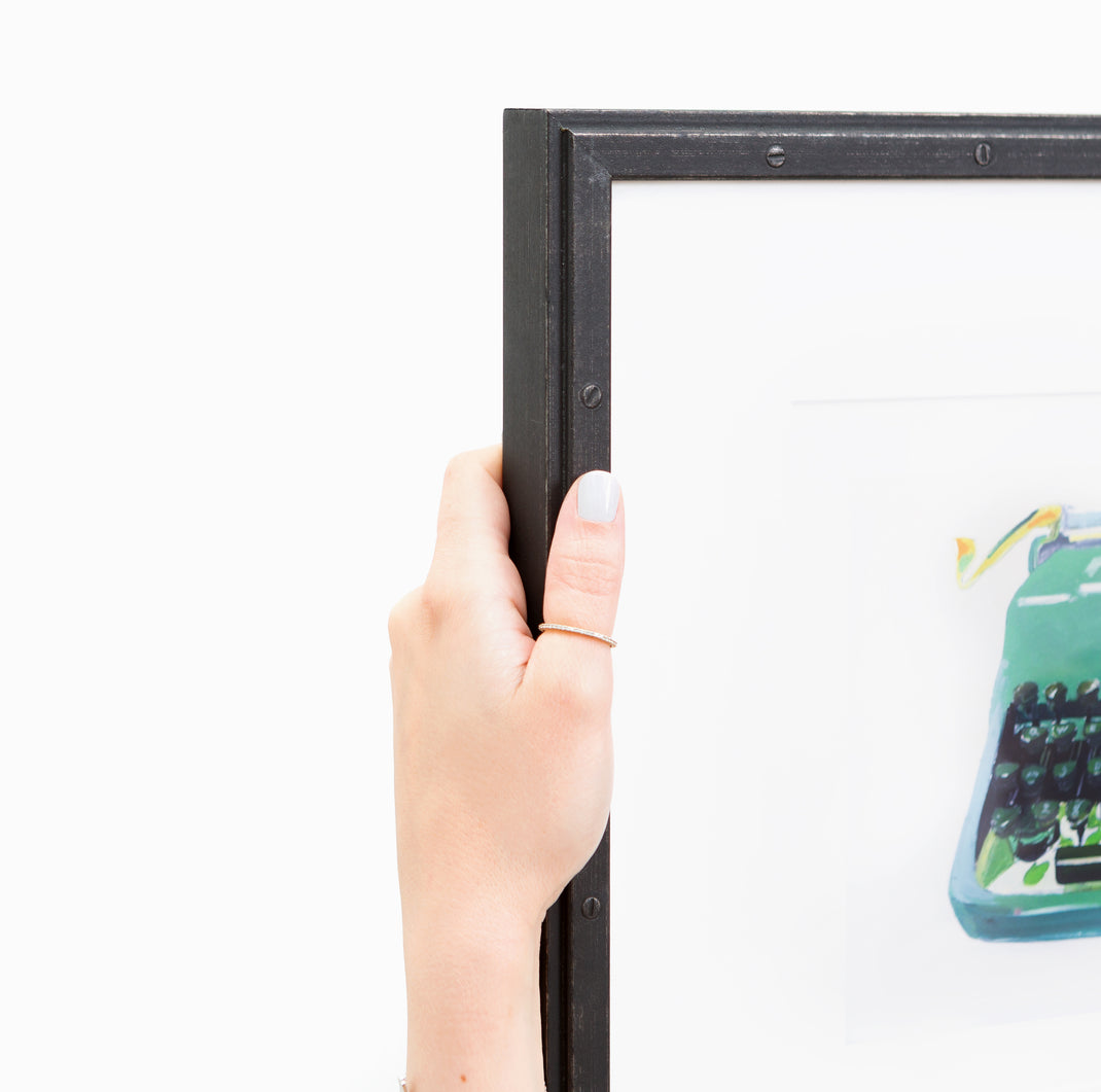 top left corner of art print of a typewriter framed in Bolton Riveted Wood Frame with a Black Steel Finish with white mat