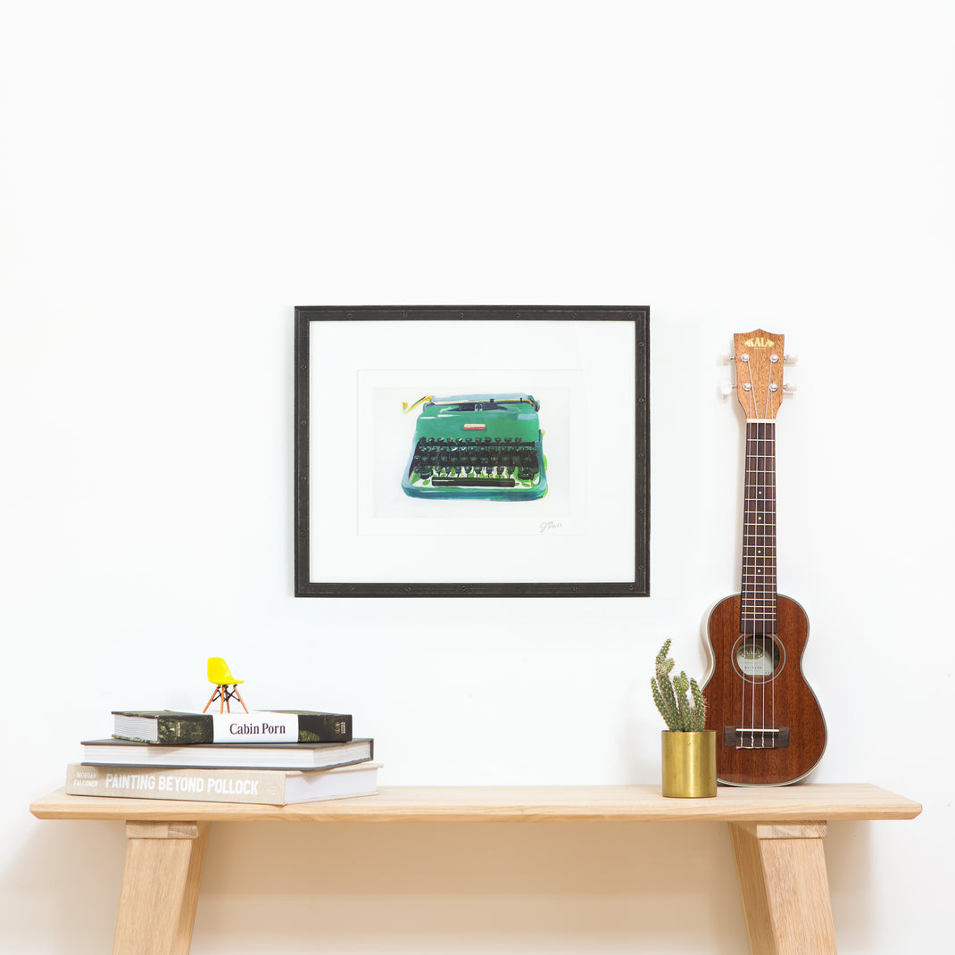 art print of a typewriter framed in Bolton Riveted Wood Frame with a Black Steel Finish with white mat hanging on a white wall above a wooden console table