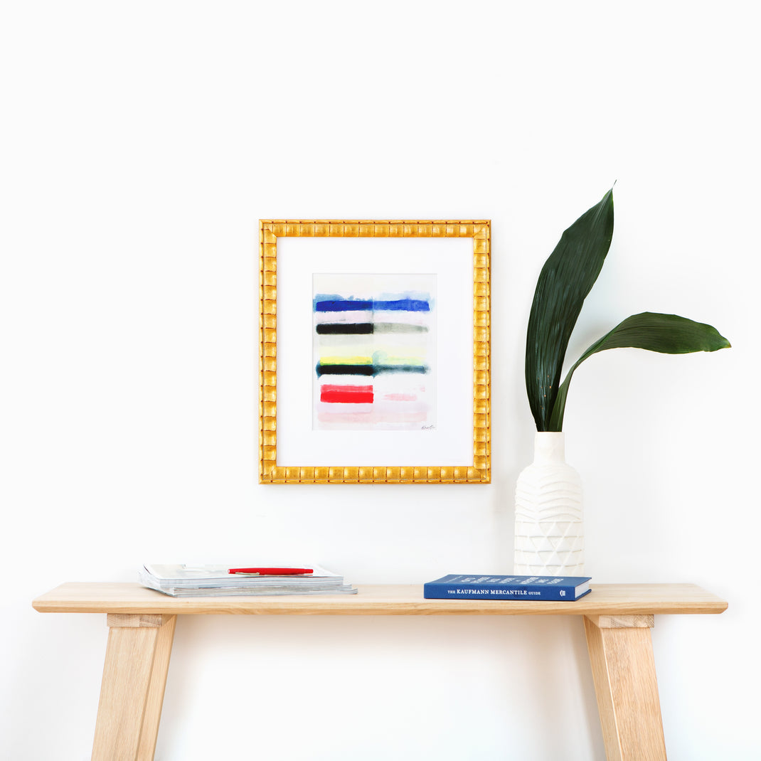 abstract art framed in rippled gold Lafayette frame with a white mat hanging on a white wall above a wood console table