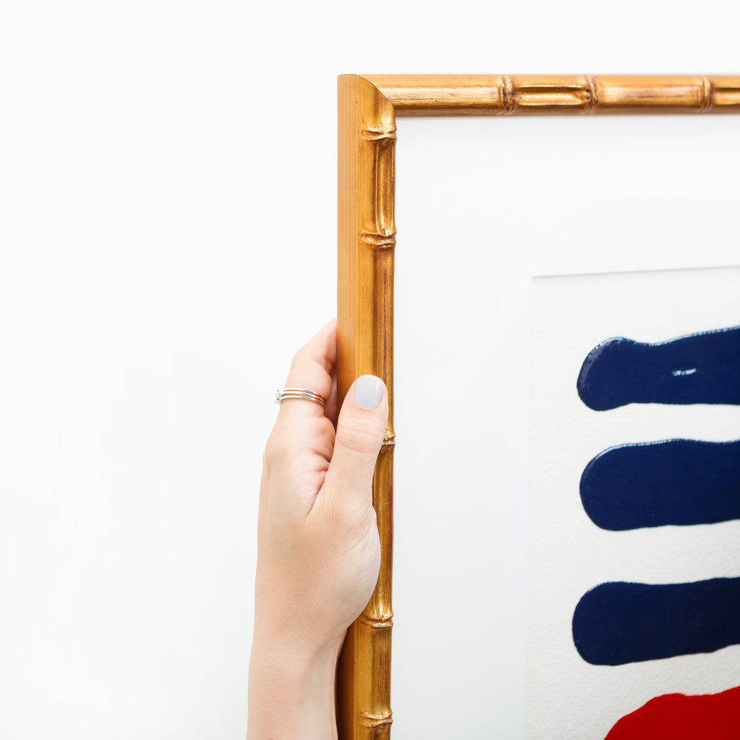 top left corner of red and blue abstract art framed in Mandalay gold bamboo frame with a white mat